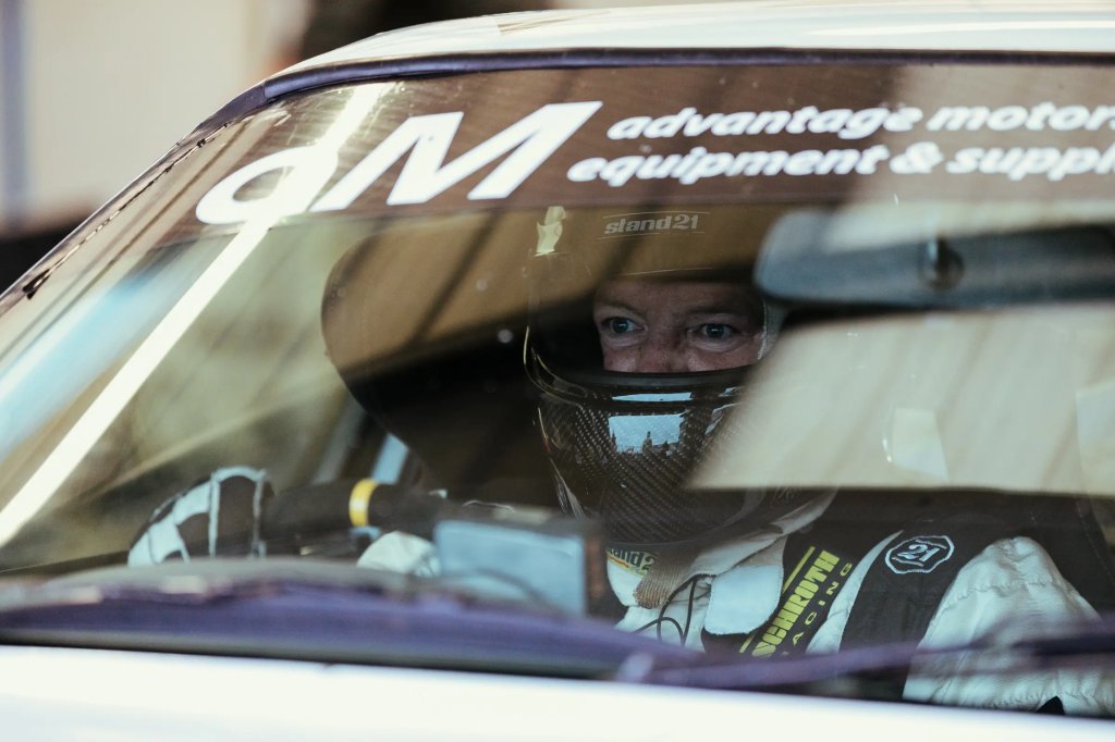 Driver wearing a helmet, seen through the windscreen of a track day car